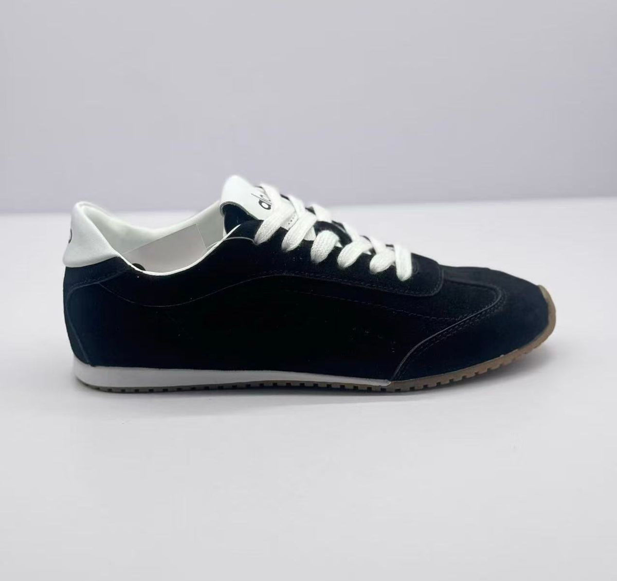 Lateral view showing the black sneaker upper, white heel detail, and textured outsole.