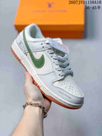 Angled side view of a white and gray low-top sneaker with green overlays, braided laces, perforated toe panel, and gum outsole.