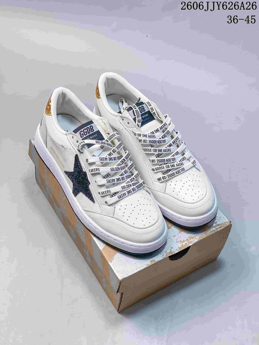 Pair of white Golden Goose sneakers with dark glitter star details, gold heel accents and a shoe box.