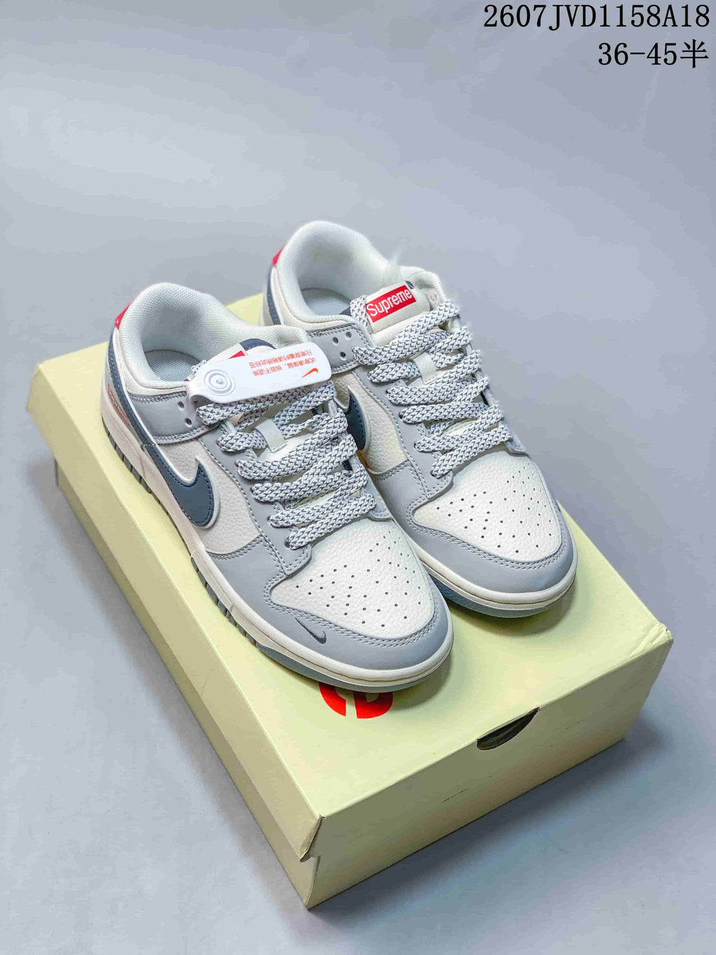 Pair of gray and white low-top sneakers with dark Swoosh details, patterned laces, and a light-colored shoe box.