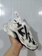 Close-up angled view of a white and black Runner sneaker showing layered panels, contrasting overlays, and a chunky sculpted sole.