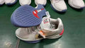 Gray low-top basketball shoes with a blue patterned outsole and red accents.