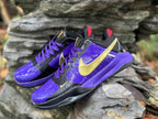 Angled view of both purple and black Nike Kobe 5 shoes with gold-colored logos and purple laces.