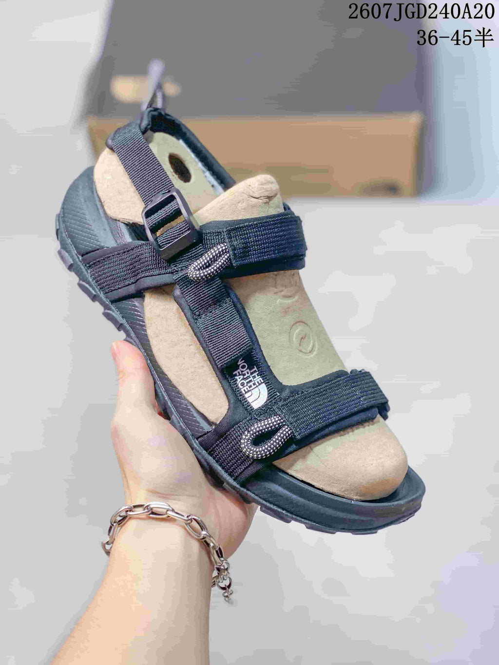 Angled front view of the black and tan sandal showing the open toe, adjustable straps, tan footbed, and lugged outsole.