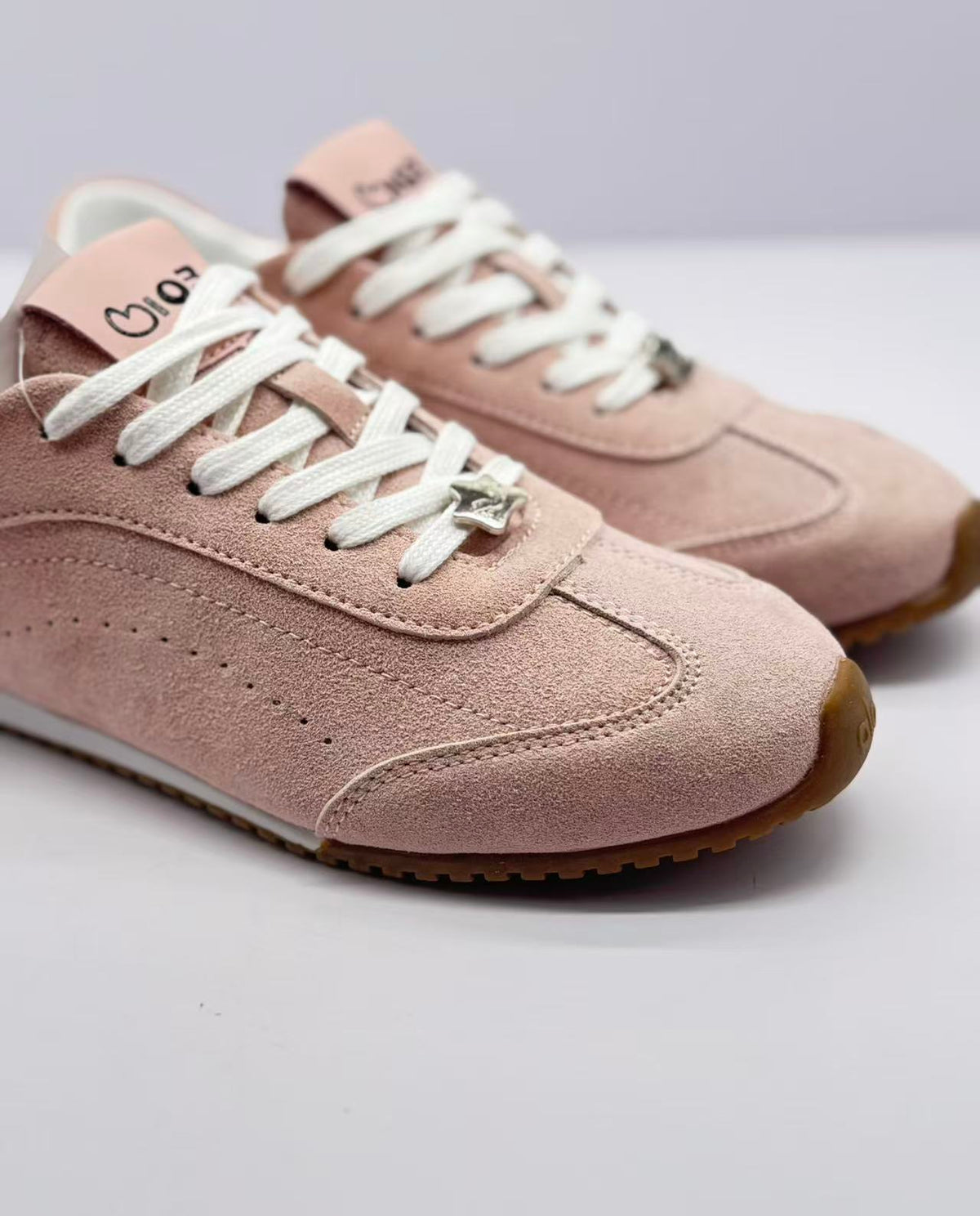 Close-up of the sneaker toe, white laces, stitched panels, and decorative lace charm.
