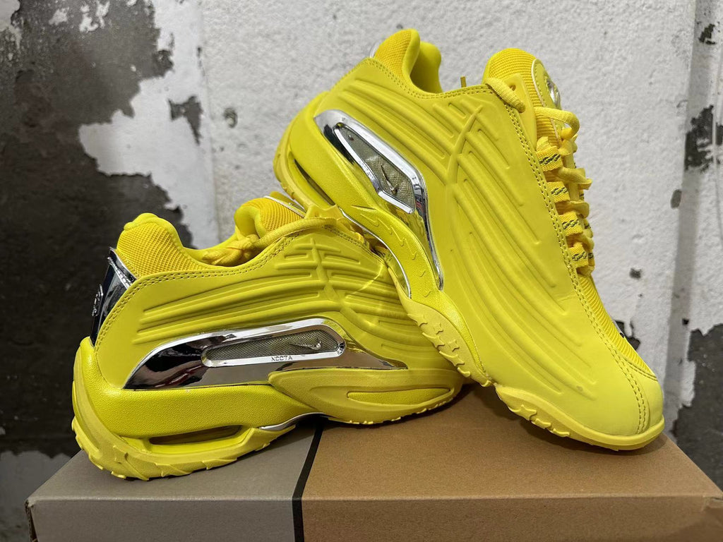 Yellow sneakers shown from the side, highlighting the sculpted panels and silver-tone accents.