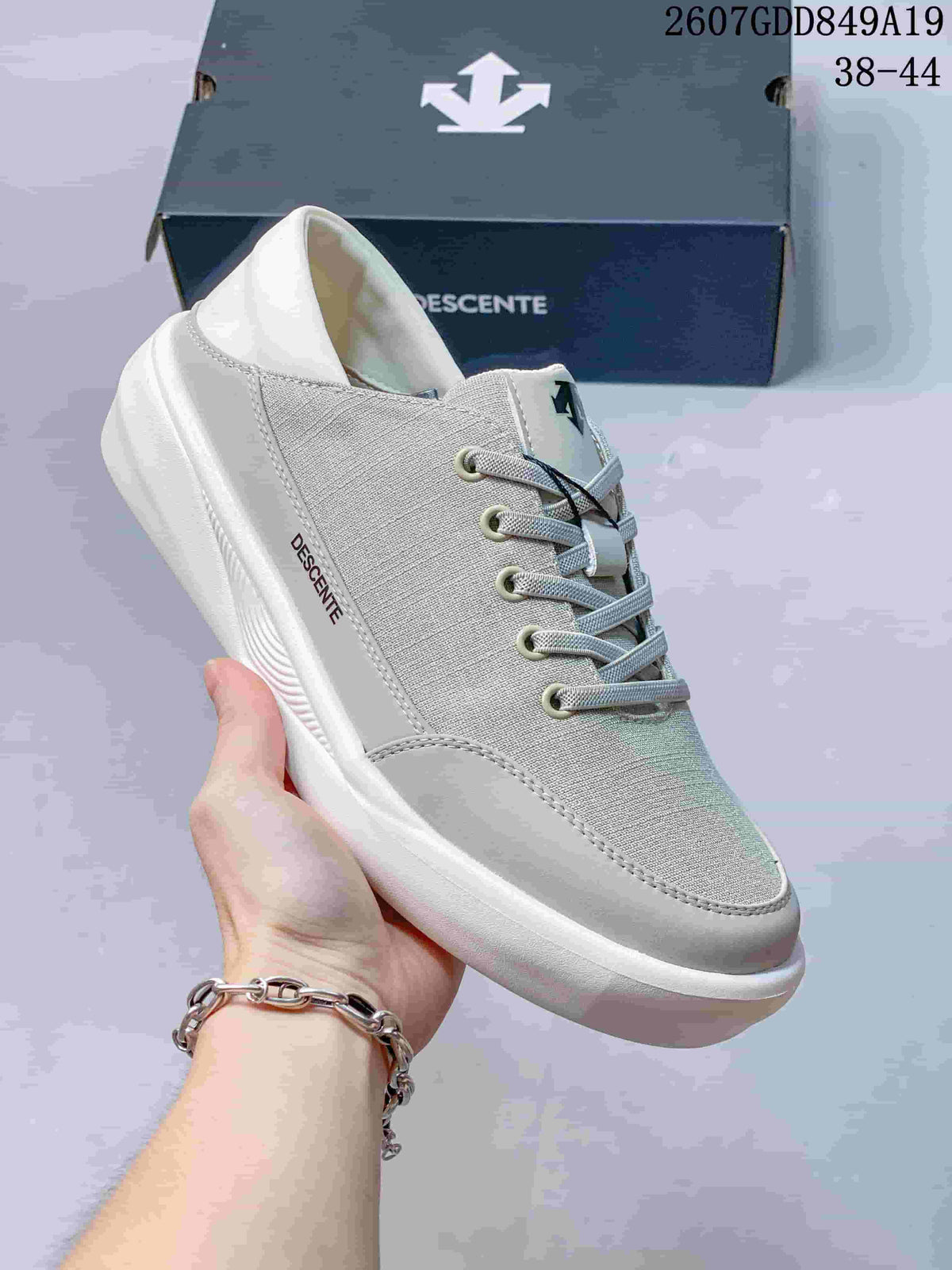 Close-up side view of a white Descente sneaker showing the textured upper, lace closure, padded collar, logo details, and white sole.