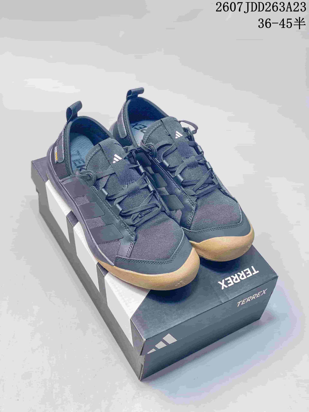 Pair of dark gray Adidas Terrex sneakers with gum-colored toe and outsole details displayed on a Terrex shoe box.