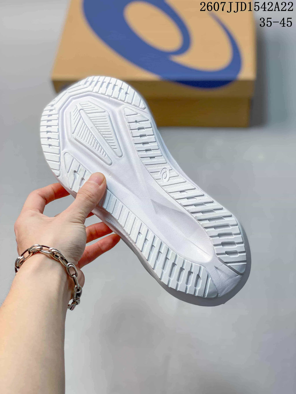 Close view of the white patterned outsole on an ASICS running shoe, with an ASICS shoebox in the background.