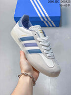 Angled side view showing the Gazelle branding, white upper, blue and lavender stripes, and translucent outsole.