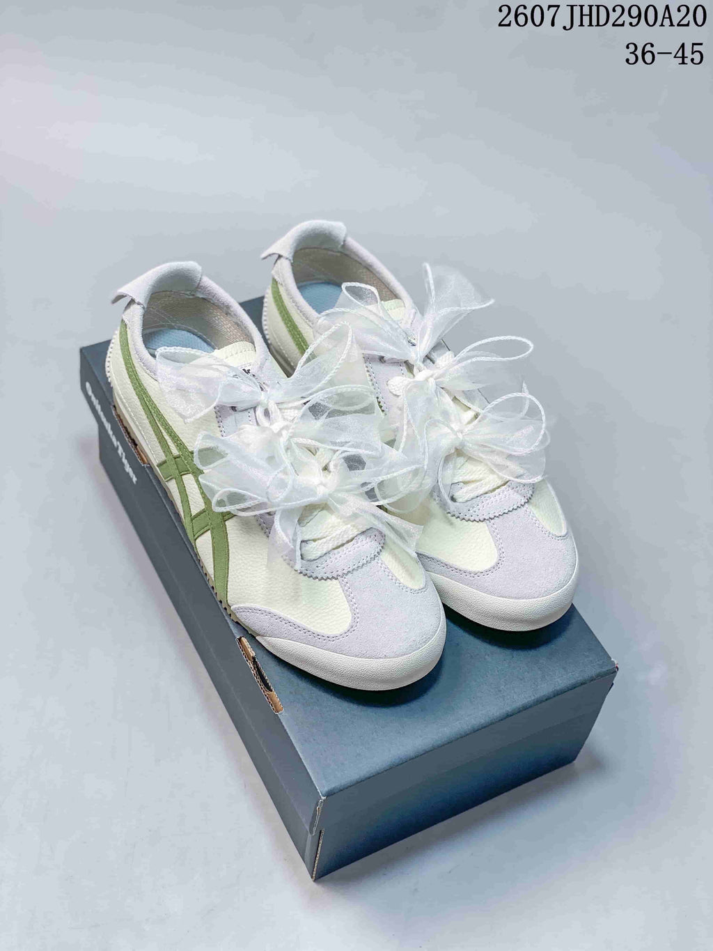 Pair of white and green Onitsuka Tiger low-top sneakers with decorative white ribbon laces displayed on a shoe box.