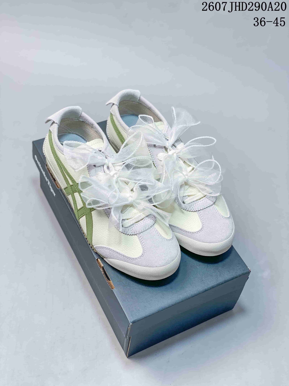 Pair of white and green Onitsuka Tiger low-top sneakers with decorative white ribbon laces displayed on a shoe box.