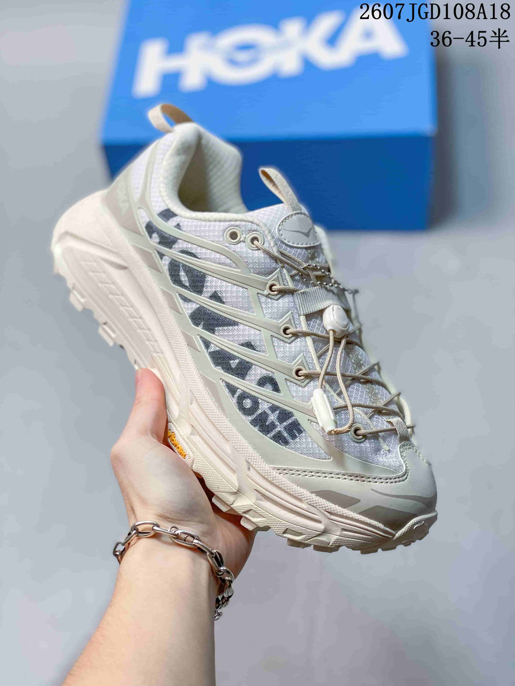 Angled side view of the white and grey HOKA sneaker showing the layered upper, pull tabs and textured outsole.