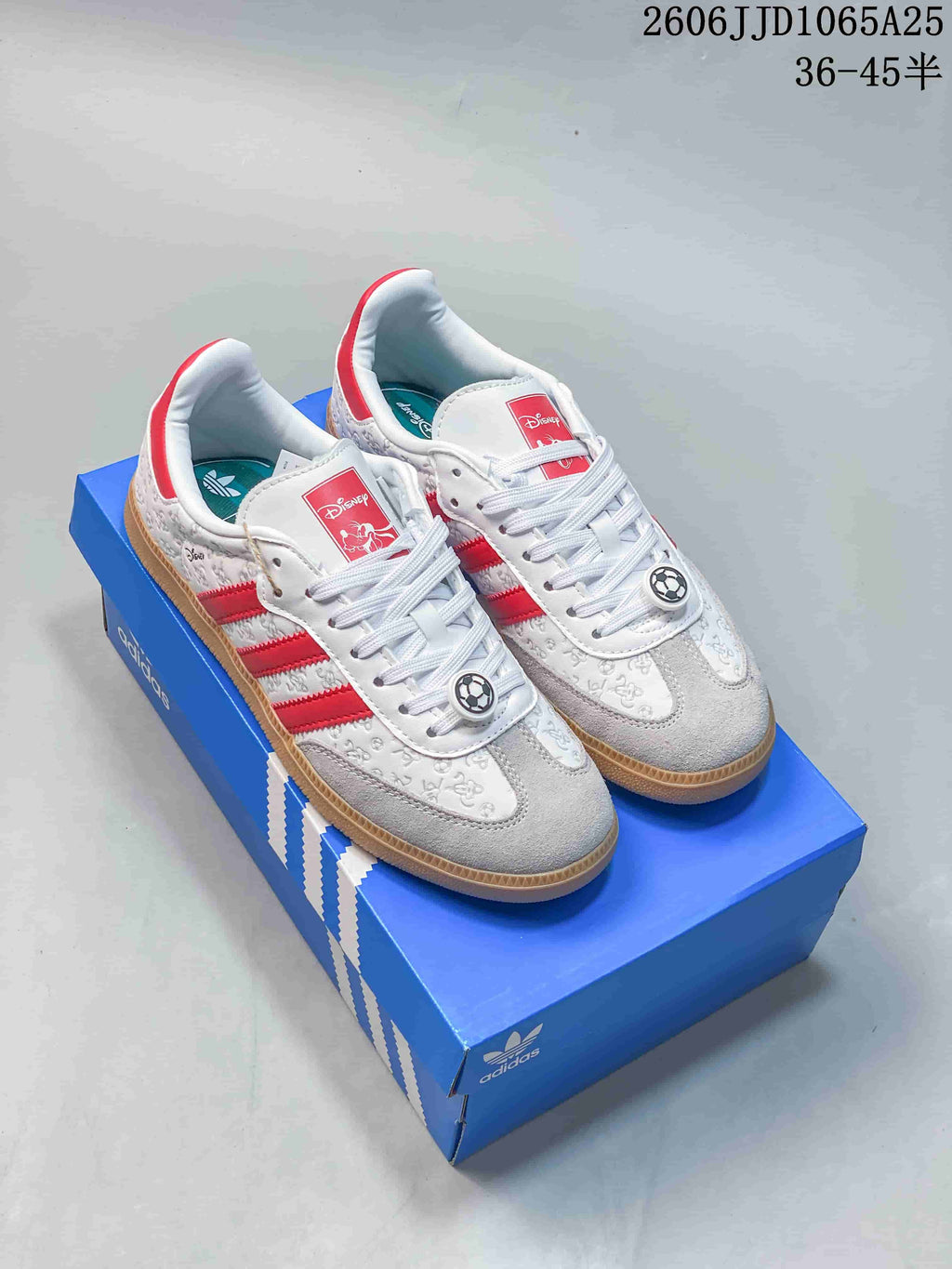 Pair of white Adidas Originals Samba-style sneakers with red stripes, Disney-themed graphics, gum soles, and a blue Adidas shoebox.