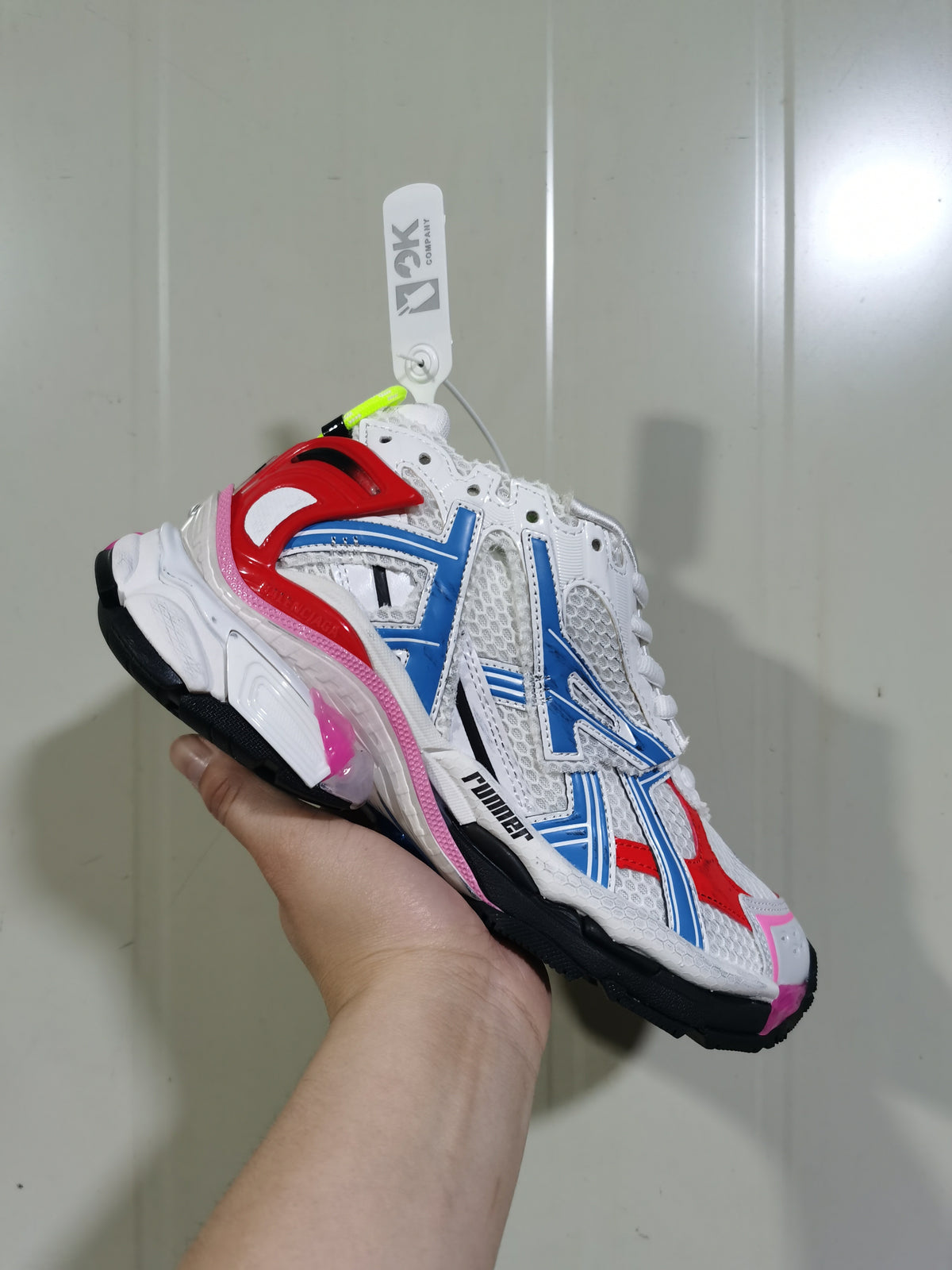 Close-up side view of a white Puma Runner sneaker with blue and red overlays, pink accents, mesh-style panels, and a black outsole.