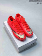 Pair of red Nike Mercurial soccer cleats displayed on a Nike shoe box, with black-and-gold swoosh detailing.