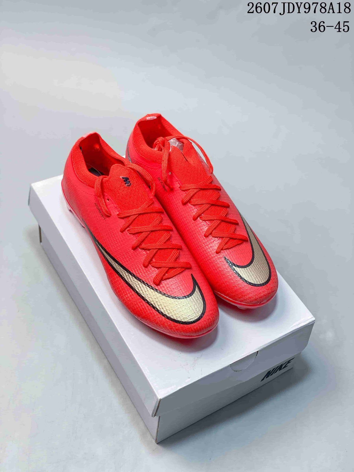 Pair of red Nike Mercurial soccer cleats displayed on a Nike shoe box, with black-and-gold swoosh detailing.