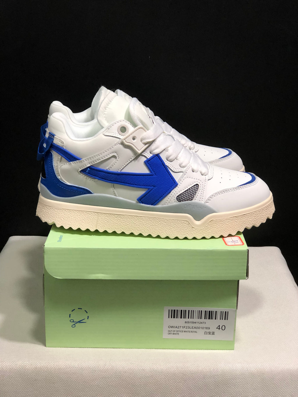 Side view of the white and royal blue sneakers showing the large blue side arrow, layered panels, and cream-colored textured outsole.