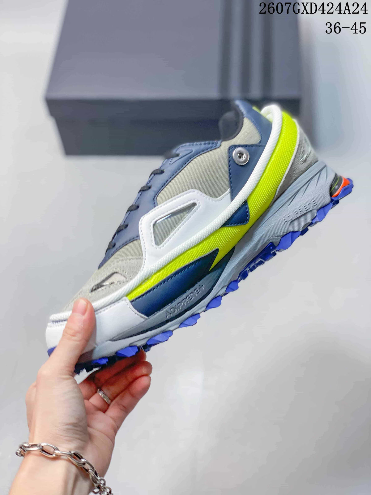 Side view highlighting the layered gray and navy upper, white structural overlays, neon yellow midsole accent and blue outsole.