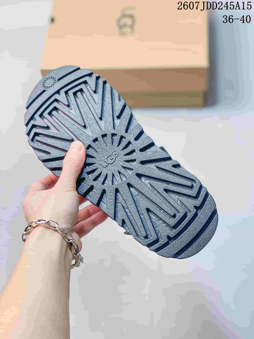 Close view of the black sandal outsole showing a radiating lugged tread pattern and UGG marking, with product code 2607JDD245A15 and size range 36–40 visible.