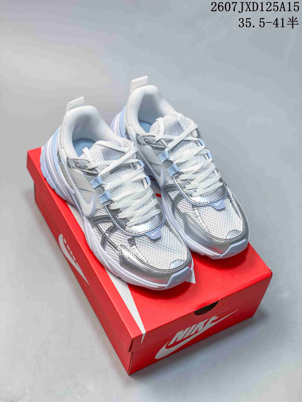 Pair of silver and white Nike V2K sneakers displayed on a red Nike shoebox.