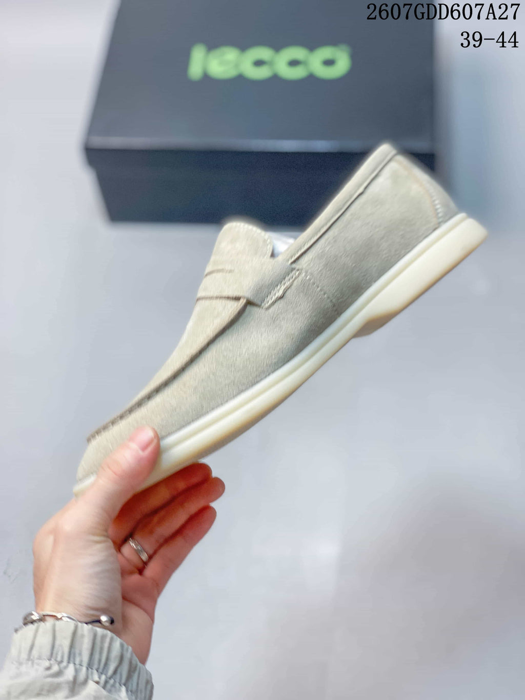 Side profile of a light beige slip-on loafer showing the apron toe, penny strap, stitching, and flat sole.