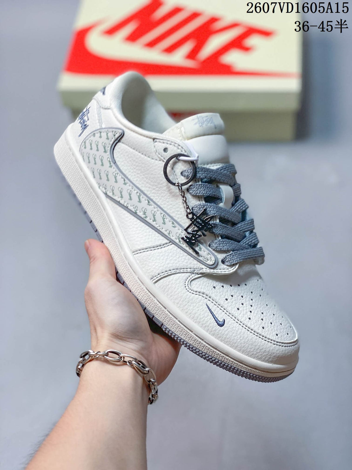 Close side view of a white sneaker with a grey Swoosh, patterned side overlay, grey laces and a textured outsole.