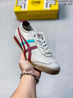 Angled side view of a white Onitsuka Tiger sneaker with burgundy and turquoise stripes and a textured gum-colored toe outsole.