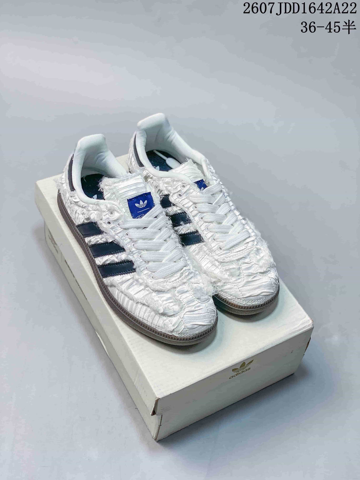 White ruched adidas Samba OG sneakers with dark contrast stripes displayed on a shoebox.