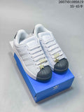 Pair of white Adidas Superstar-style sneakers with black shell toes, gold-toned lace details, and a blue Adidas shoebox.