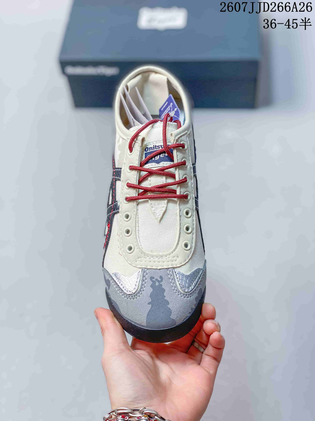 Front view of the sneaker showing the cream lace panel, red laces, navy branding, and gray patterned toe.