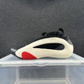 Side view of a black low-top sneaker with a light-colored sculpted side panel and red accent