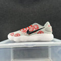 Side view of a light gray Nike low-top sneaker with red dragon-inspired graphics and laces, a black Swoosh, and a white ridged sole.