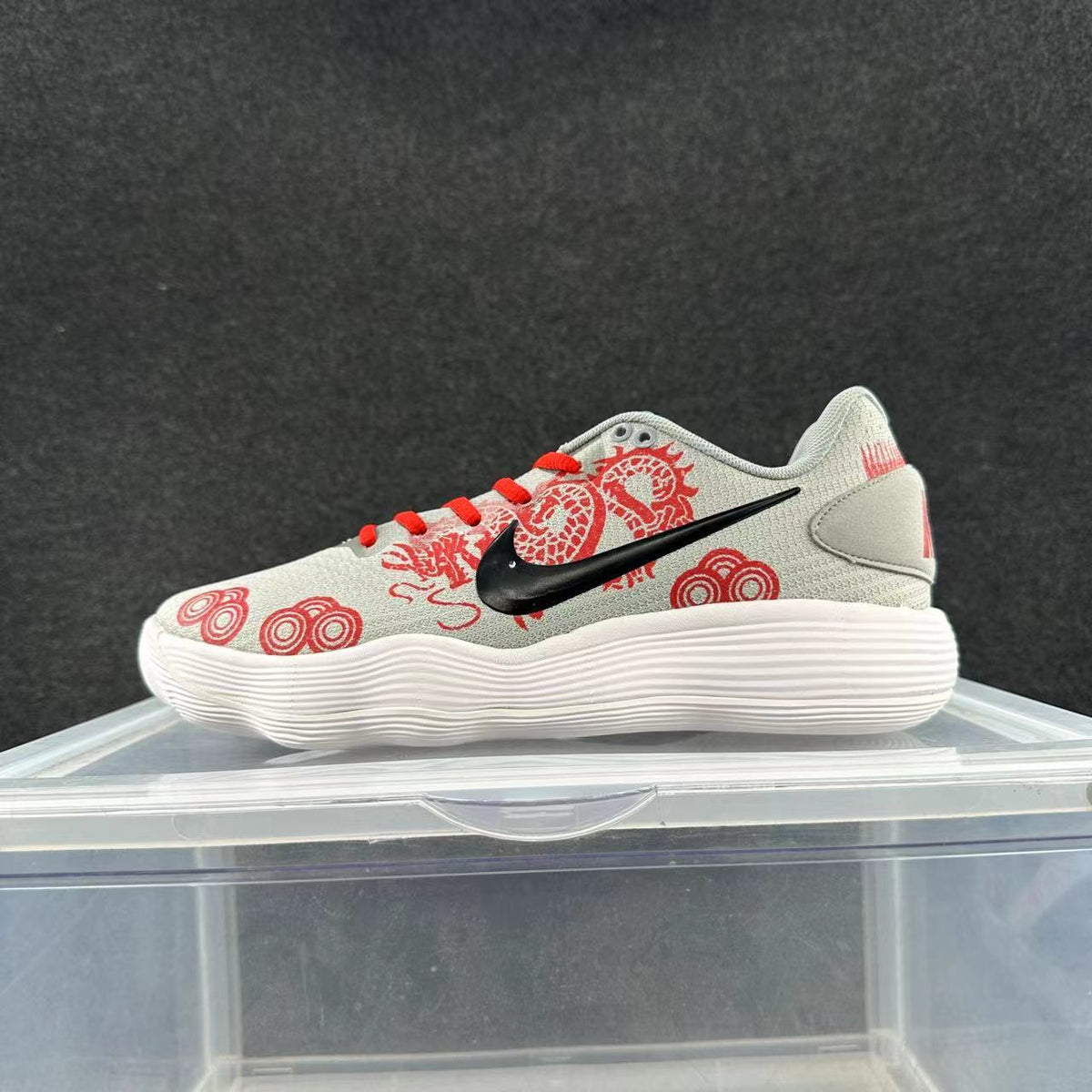 Side view of a light gray Nike low-top sneaker with red dragon-inspired graphics and laces, a black Swoosh, and a white ridged sole.