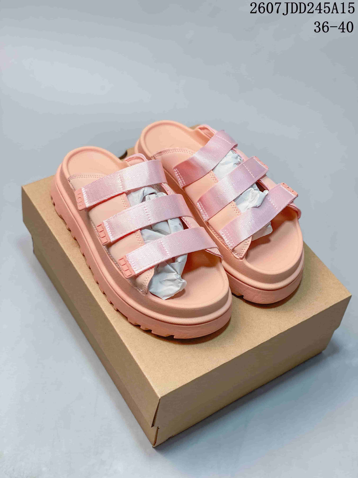Pair of pink UGG slide sandals displayed on a box, showing three straps and the open-toe design.