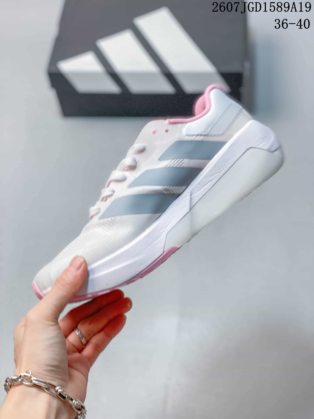Side profile of the white trainer showing gray stripe overlays, a raised heel section and pink outsole details.