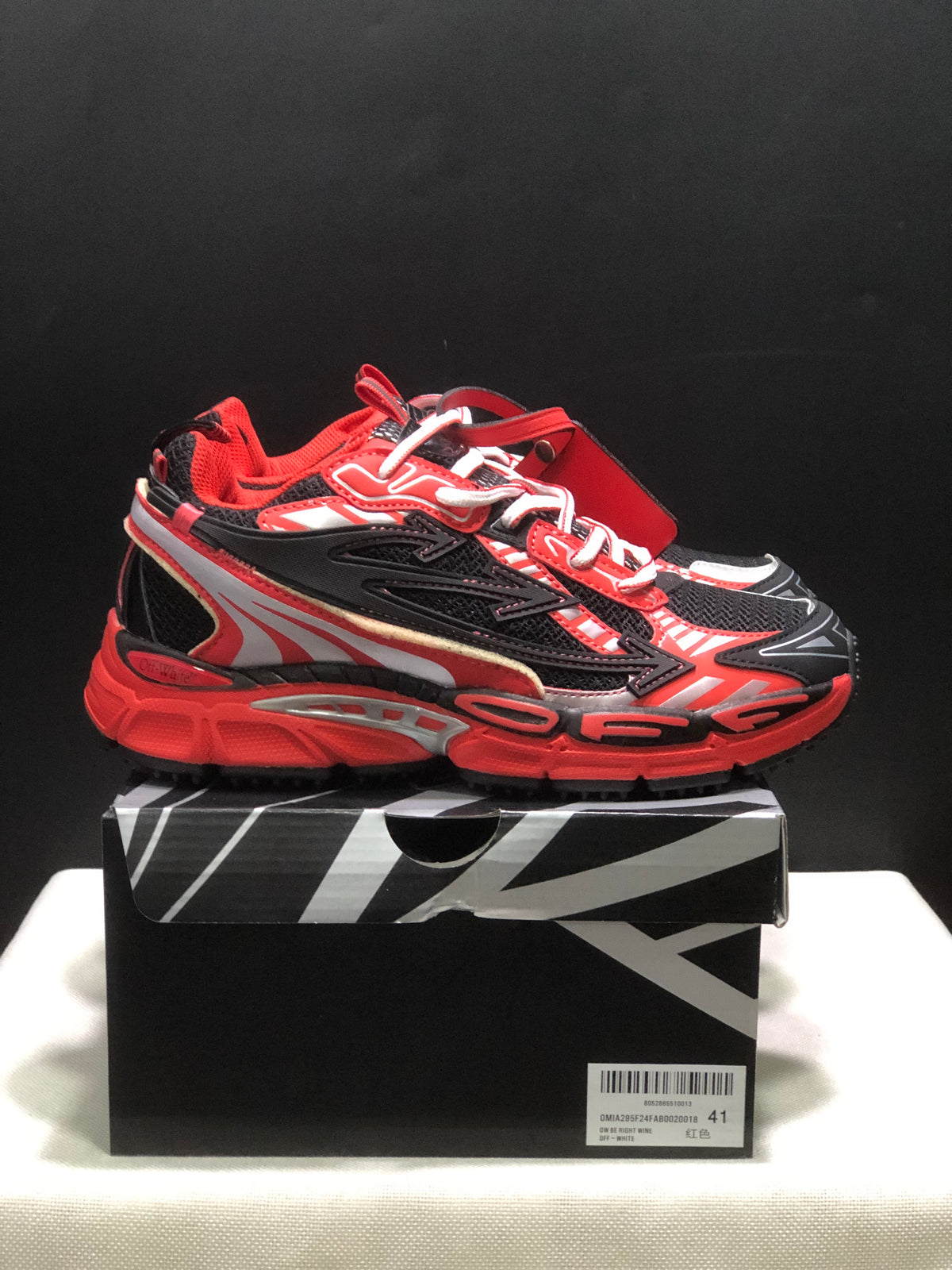Side view of the red, black, and white lace-up sneakers showing layered panels, mesh sections, and a chunky sole.