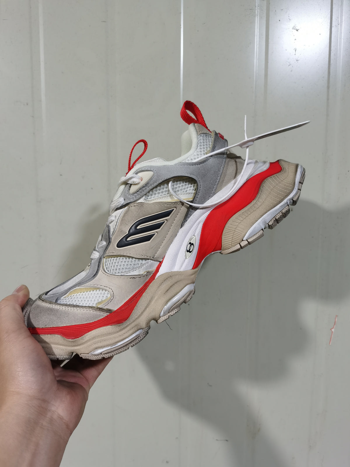 Angled view of a grey, beige, white and orange layered sneaker with mesh panels, contrasting overlays and pull tabs.