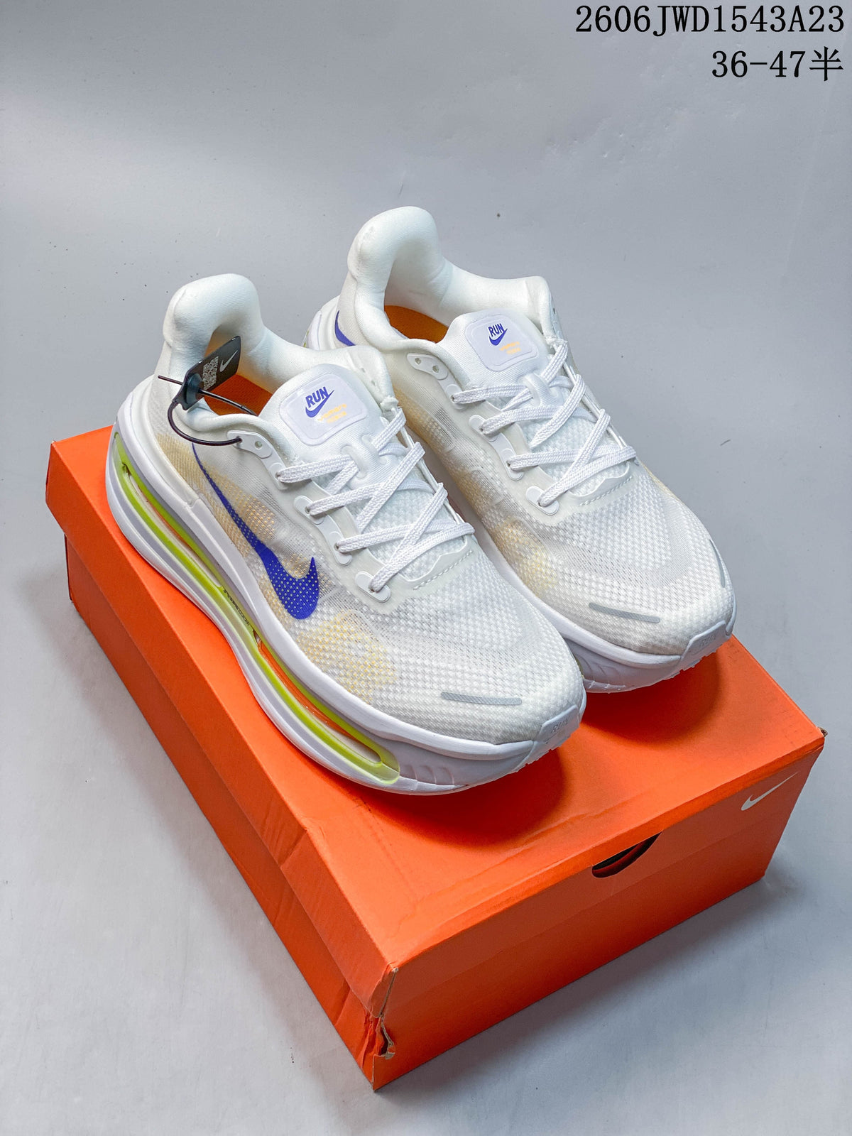 White Nike Vomero Premium running shoes with purple accents and lime and orange midsole details, shown on an orange shoe box.