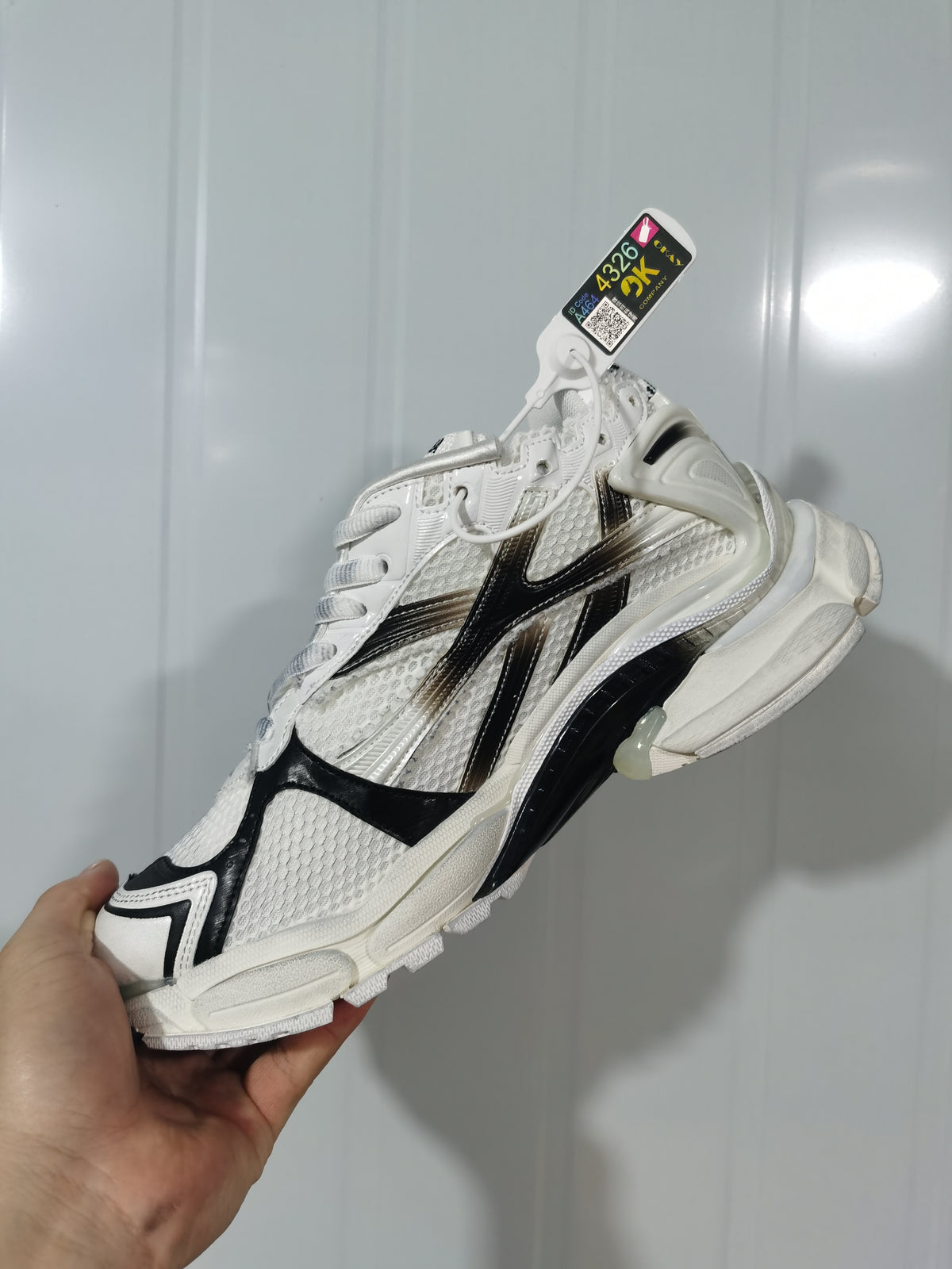 Side view of the white and black sneaker showing the layered upper, lace fastening, and sculpted heel structure.