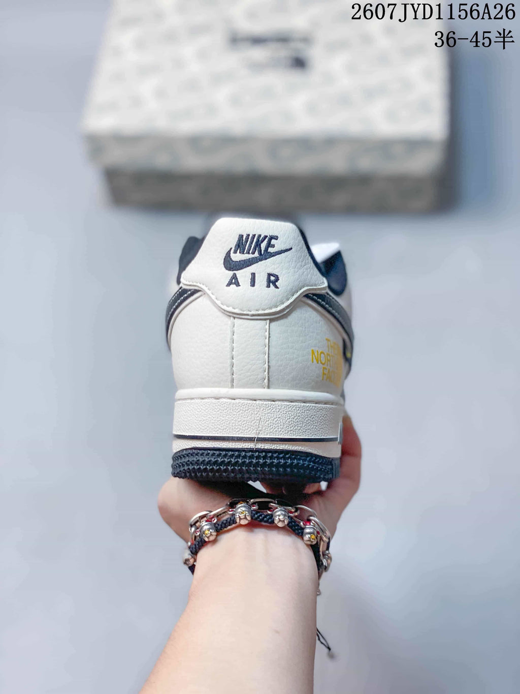 Rear view of a white and navy Nike Air Force 1 sneaker showing the Nike Air heel tab and yellow side lettering.