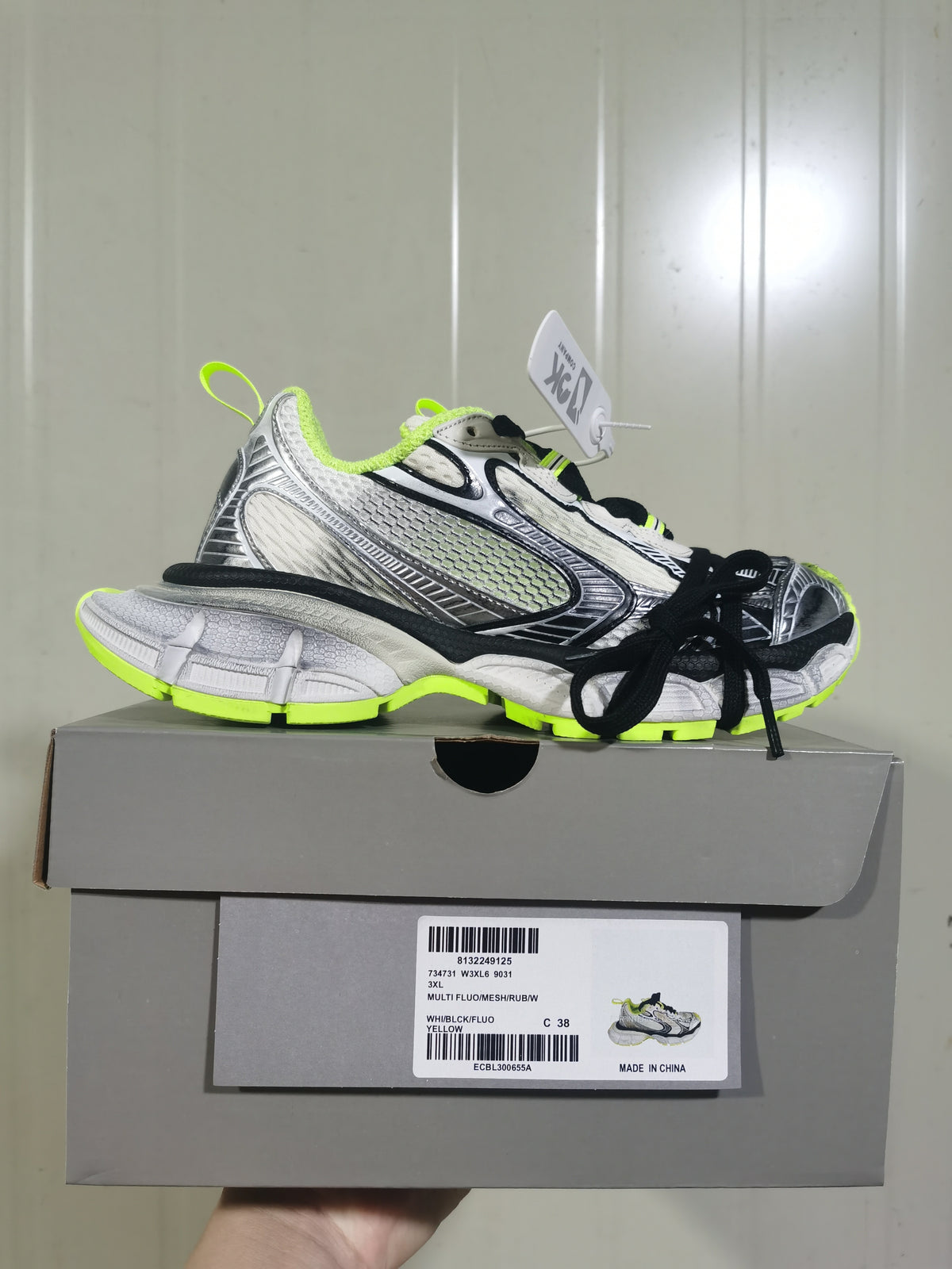 Side view of the Nike sneaker resting on its box; the label shows size C 38 and color text including WH/BLCK/FLUO YELLOW.