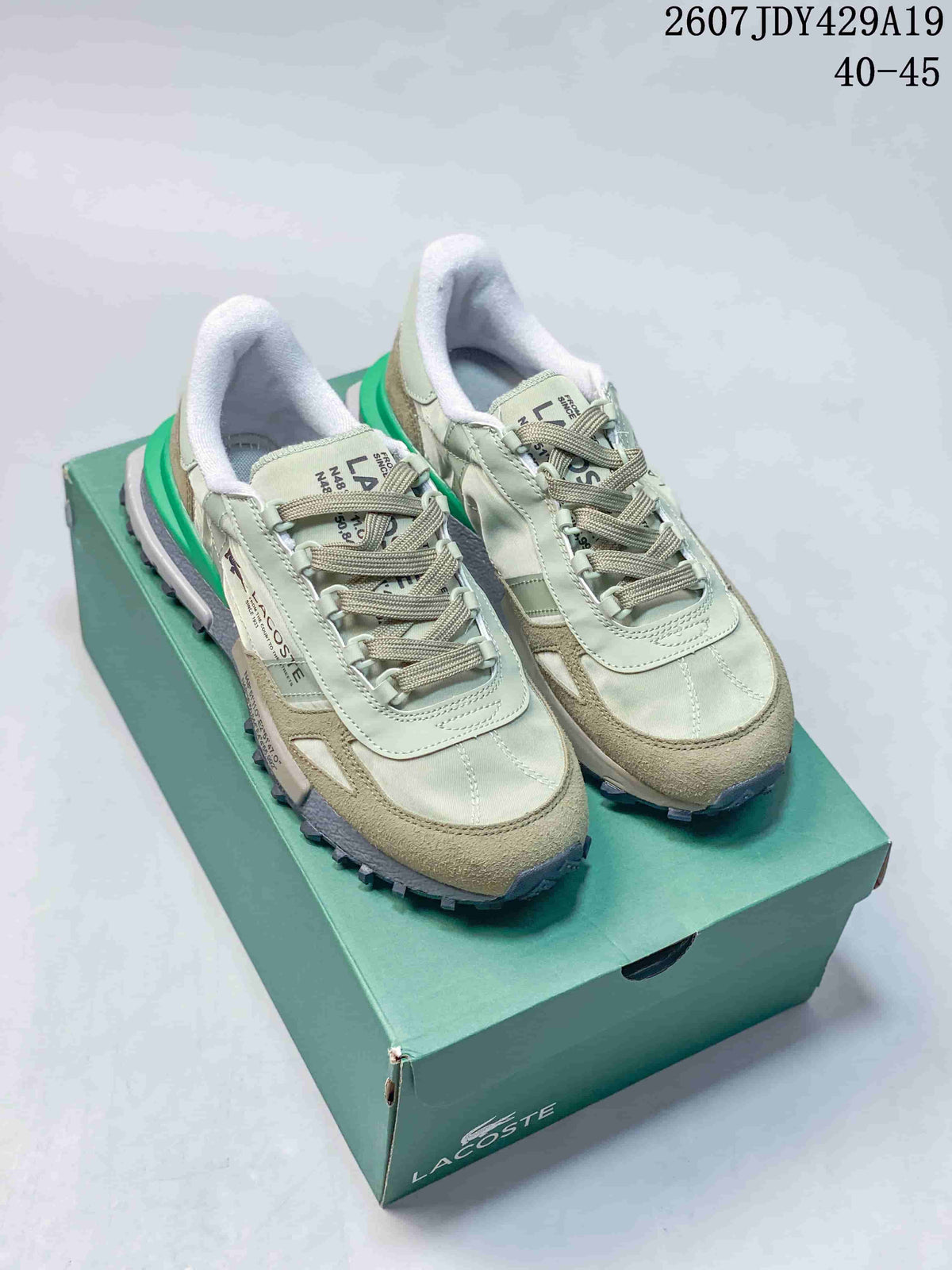 Pair of pale green and khaki Lacoste low-top sneakers displayed on a green shoe box.