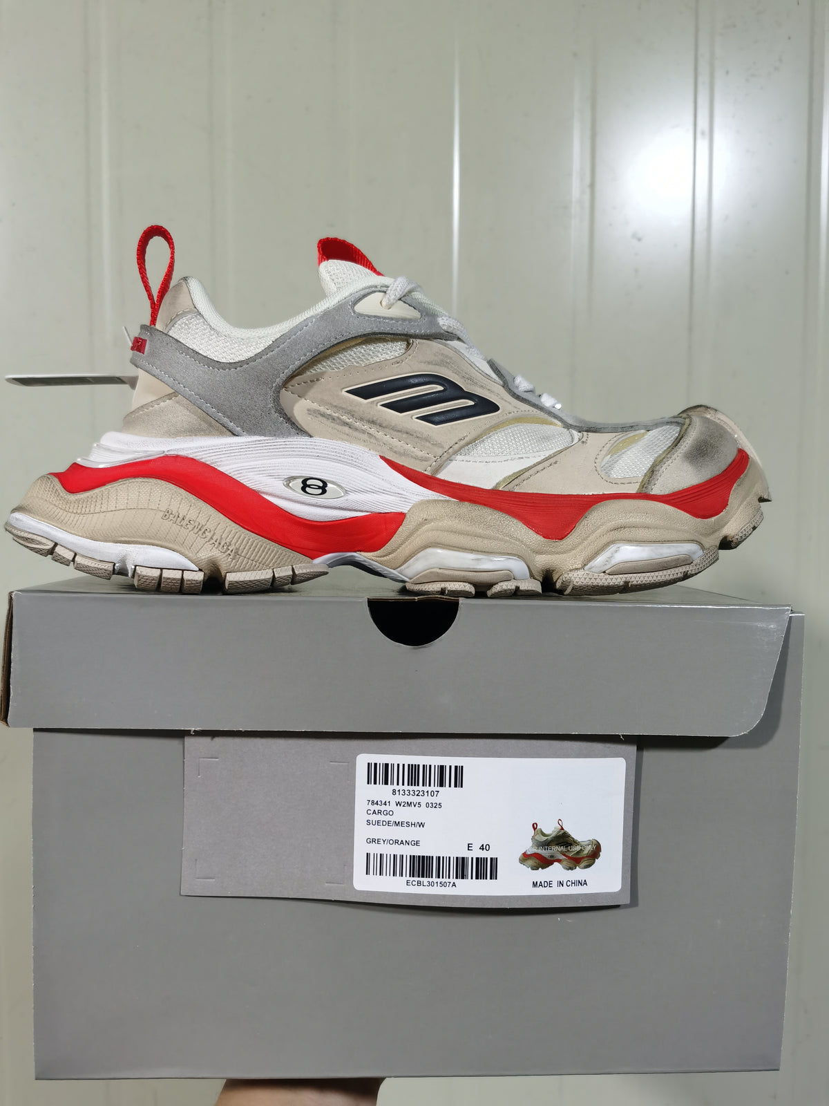 Side view of the sneaker resting on its box, showing the sculpted sole, layered upper and box label marked CARGO and GREY/ORANGE.