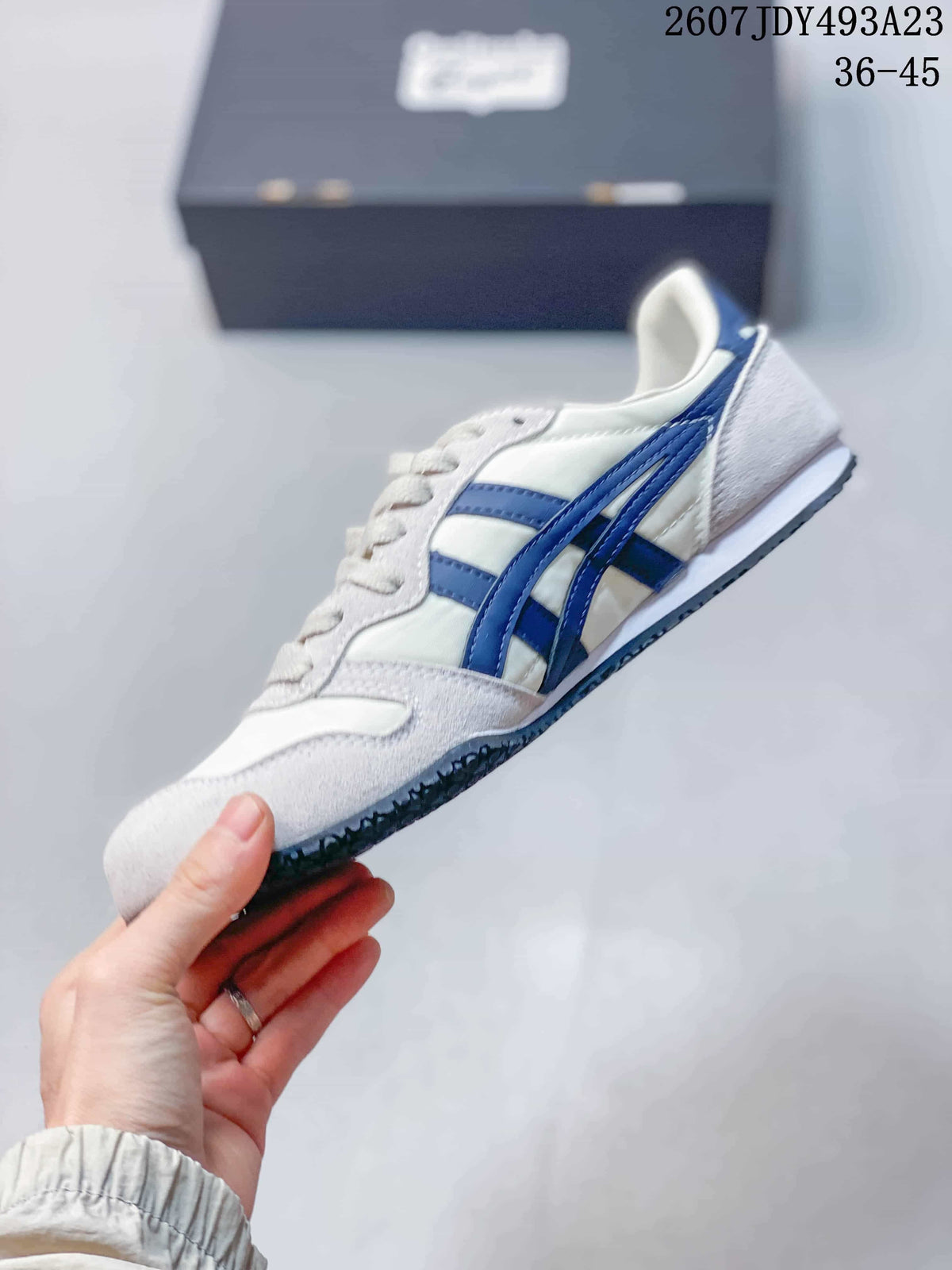 Side profile of the white sneaker with layered blue side stripes, white midsole and dark textured outsole; overlay shows model code 2607JDY493A23 and size range 36–45.