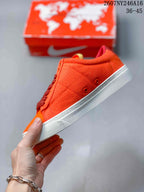 Side view of the orange low-top sneaker showing stitched panels, dark red laces, and an embossed white midsole edge.