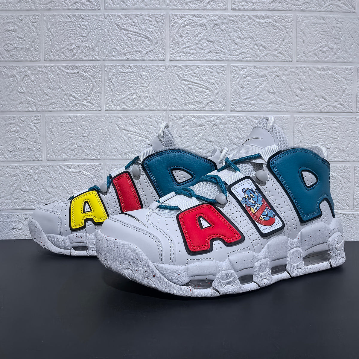 Pair of sneakers showing white uppers with red, yellow and blue letter accents