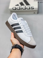 Angled side view of the white sneaker with black stripes and a brown gum-colored outsole.