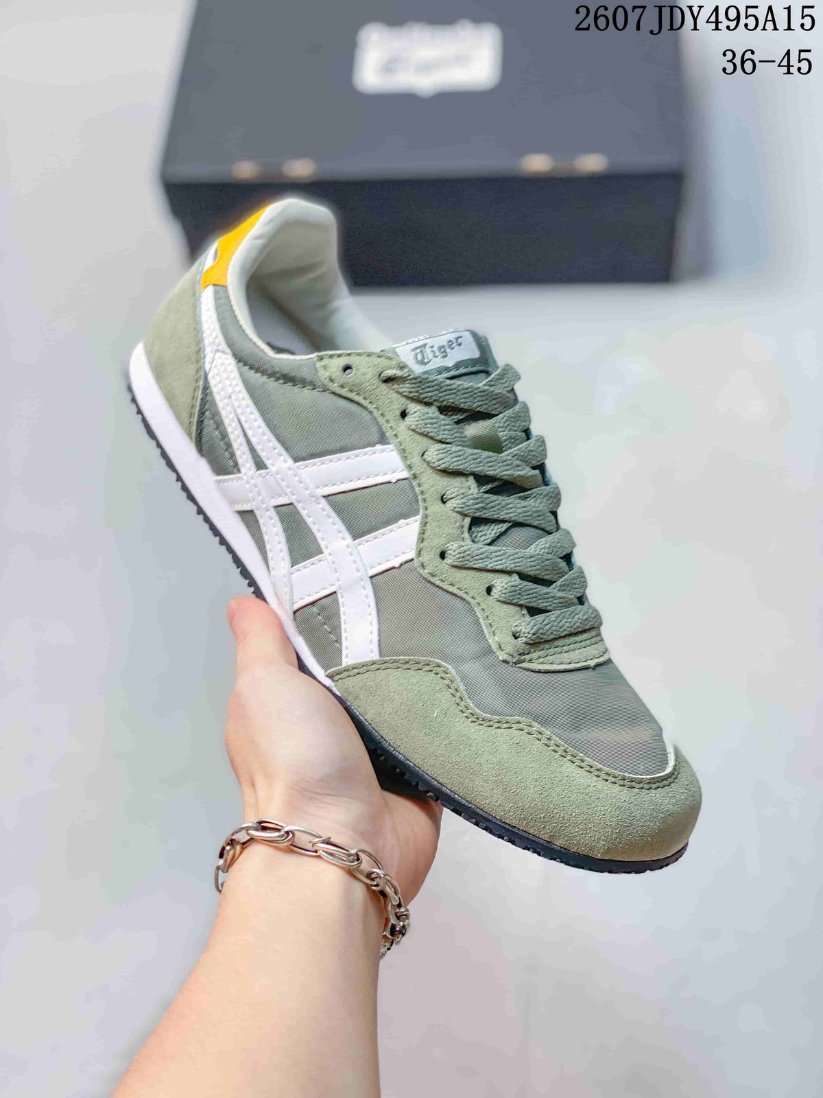 Angled side view of a green and white Onitsuka Tiger Serrano sneaker showing the low-profile silhouette, contrasting side stripes, and dark outsole.