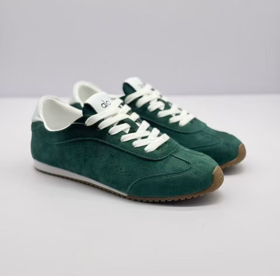 Pair of green Alo sneakers shown from a front three-quarter angle with white laces and brown toe edges.